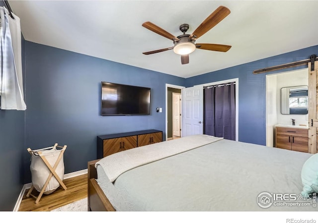 bedroom with a barn door, wood finished floors, baseboards, and a ceiling fan