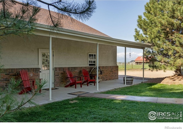 rear view of house with brick siding, stucco siding, a patio, and a lawn