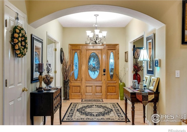 foyer featuring arched walkways, a chandelier, and light wood-style flooring