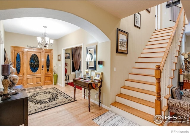 foyer entrance featuring arched walkways, light wood-style floors, a chandelier, stairs, and baseboards