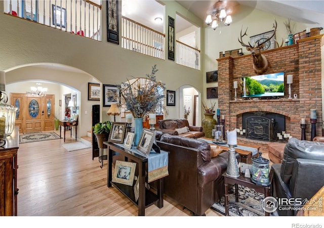 living room with arched walkways, a brick fireplace, wood finished floors, a towering ceiling, and a ceiling fan