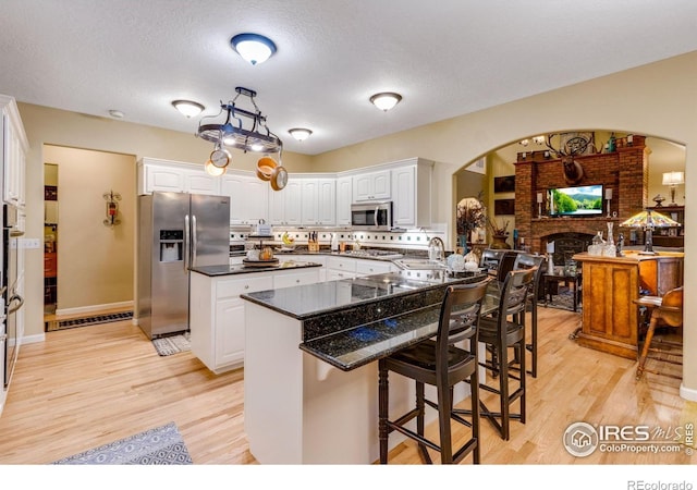 kitchen featuring stainless steel appliances, arched walkways, light wood-style floors, a breakfast bar, and a textured ceiling