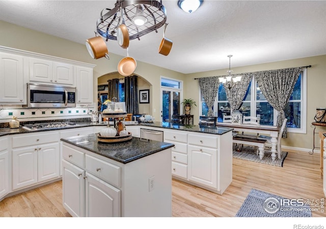 kitchen with appliances with stainless steel finishes, a center island, a chandelier, a peninsula, and light wood-style floors