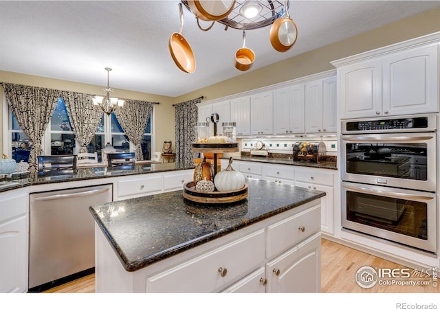 kitchen featuring stainless steel appliances, a chandelier, white cabinetry, light wood finished floors, and decorative light fixtures