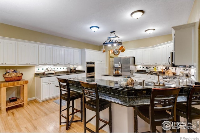 kitchen with freestanding refrigerator, a kitchen breakfast bar, a sink, a peninsula, and light wood-style flooring