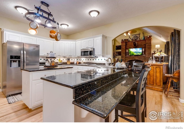 kitchen featuring stainless steel appliances, arched walkways, light wood-style flooring, white cabinets, and a textured ceiling