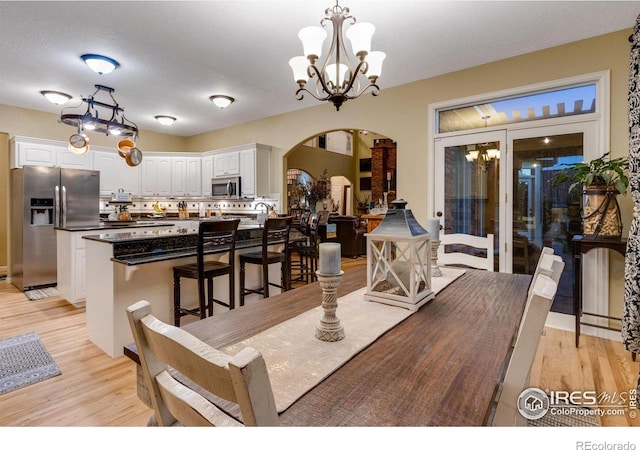 dining space with arched walkways, light wood-style floors, and a chandelier