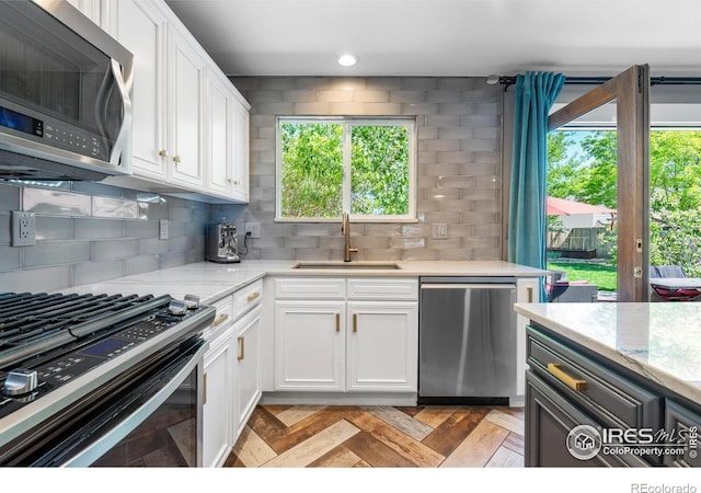 kitchen featuring appliances with stainless steel finishes, a sink, backsplash, white cabinets, and light stone countertops
