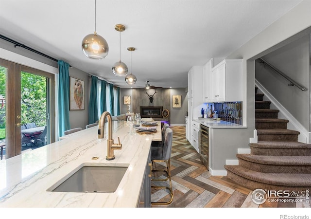 kitchen with a sink, open floor plan, light stone countertops, white cabinets, and hanging light fixtures