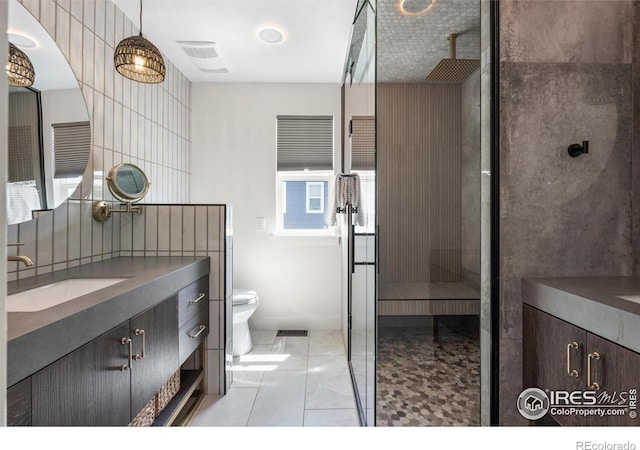 full bathroom with vanity, a walk in shower, toilet, tile patterned floors, and tile walls
