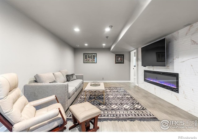living room featuring recessed lighting, a glass covered fireplace, wood finished floors, and baseboards
