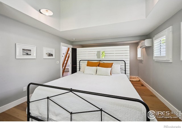 bedroom featuring a wall mounted air conditioner, wood finished floors, and baseboards