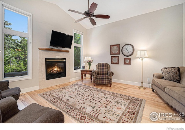 living room with a tiled fireplace, lofted ceiling, baseboards, wood finished floors, and ceiling fan