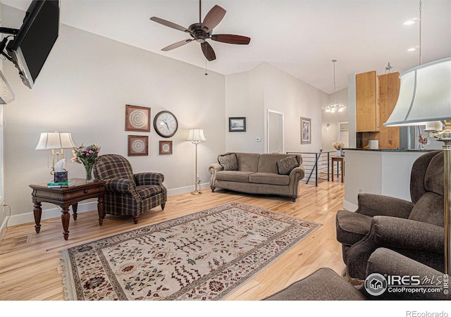 living area with light wood-style flooring, a ceiling fan, baseboards, a chandelier, and vaulted ceiling