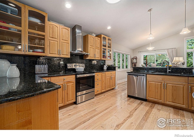 kitchen with wall chimney range hood, appliances with stainless steel finishes, a sink, light wood-style floors, and tasteful backsplash