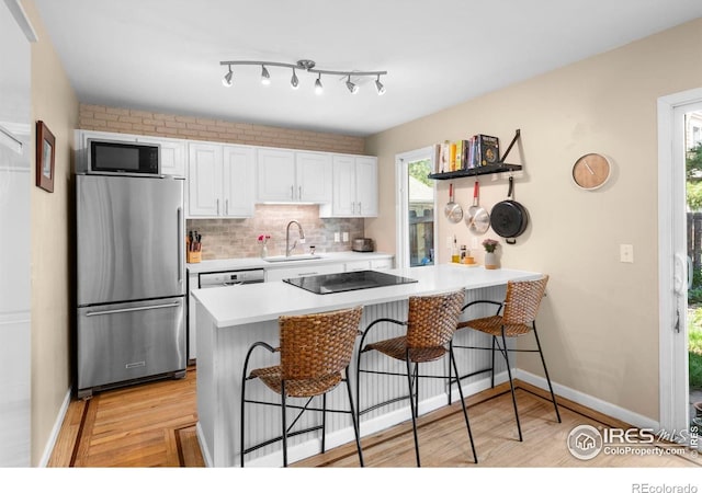 kitchen featuring freestanding refrigerator, a sink, black electric stovetop, and light wood-style flooring
