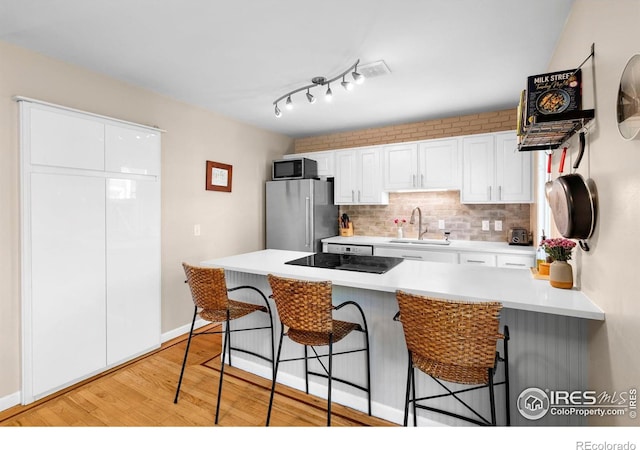kitchen with appliances with stainless steel finishes, a sink, a kitchen breakfast bar, light wood-style flooring, and white cabinets
