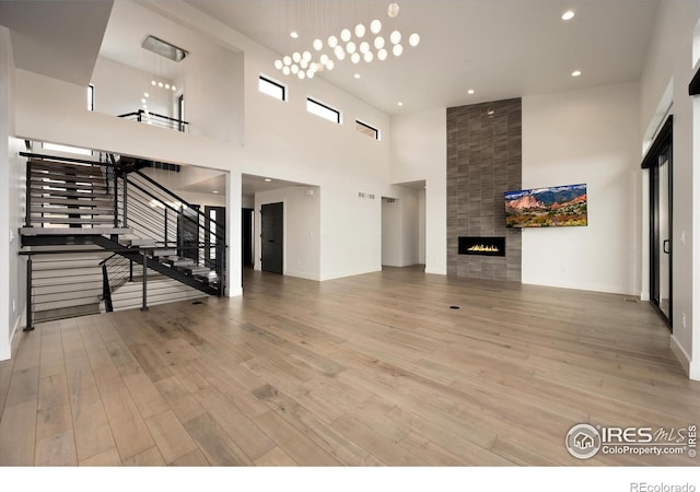 unfurnished living room with a towering ceiling, a tile fireplace, wood finished floors, stairs, and recessed lighting