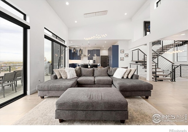 living room with a towering ceiling, light wood-style flooring, stairway, and recessed lighting