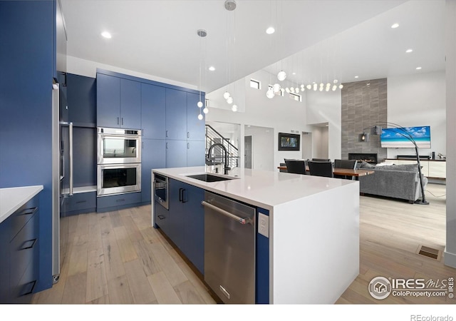 kitchen with appliances with stainless steel finishes, a sink, blue cabinets, light wood-style floors, and a high ceiling