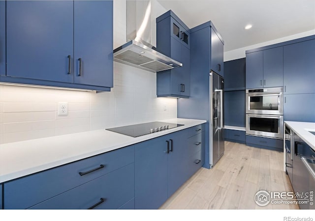 kitchen with wall chimney exhaust hood, blue cabinets, light wood finished floors, appliances with stainless steel finishes, and recessed lighting