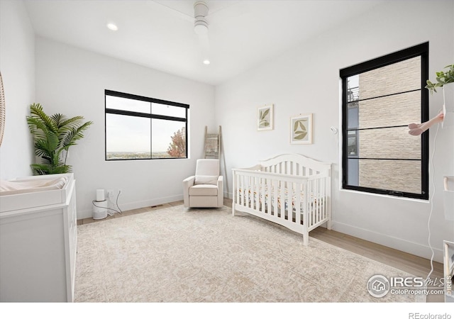 bedroom with wood finished floors, a nursery area, baseboards, recessed lighting, and ceiling fan