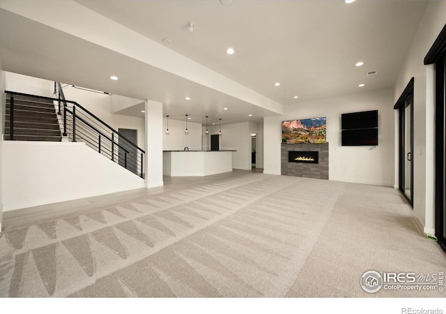 unfurnished living room with light carpet, recessed lighting, a tiled fireplace, stairs, and baseboards