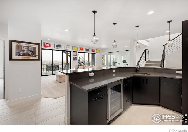 kitchen featuring beverage cooler, dark cabinets, a sink, dark countertops, and recessed lighting