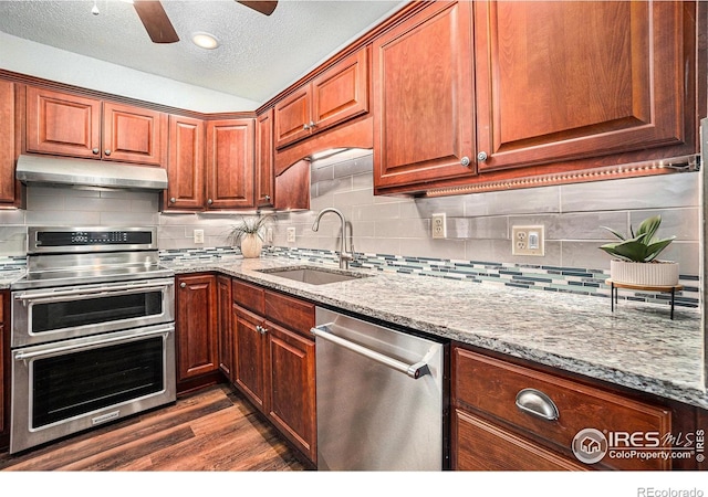 kitchen featuring under cabinet range hood, appliances with stainless steel finishes, a sink, light stone counters, and dark wood-style floors