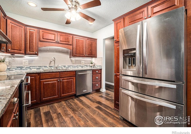 kitchen with stainless steel appliances, ceiling fan, a sink, dark wood-style floors, and decorative backsplash