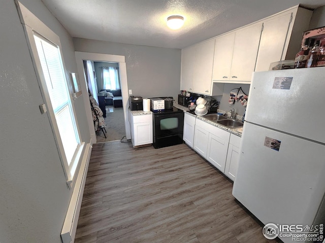 kitchen featuring freestanding refrigerator, black / electric stove, light wood-style floors, white cabinetry, and a sink
