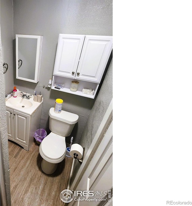 half bath with wood finished floors, toilet, and vanity