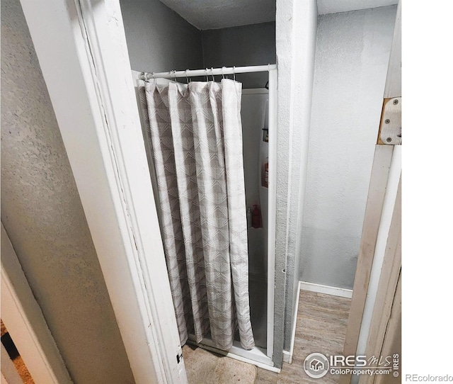 bathroom with curtained shower, wood finished floors, and a textured wall