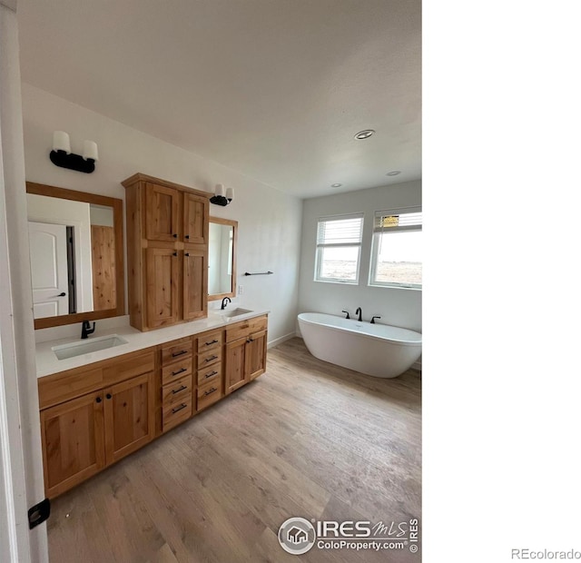 full bath featuring wood finished floors, double vanity, and a freestanding tub