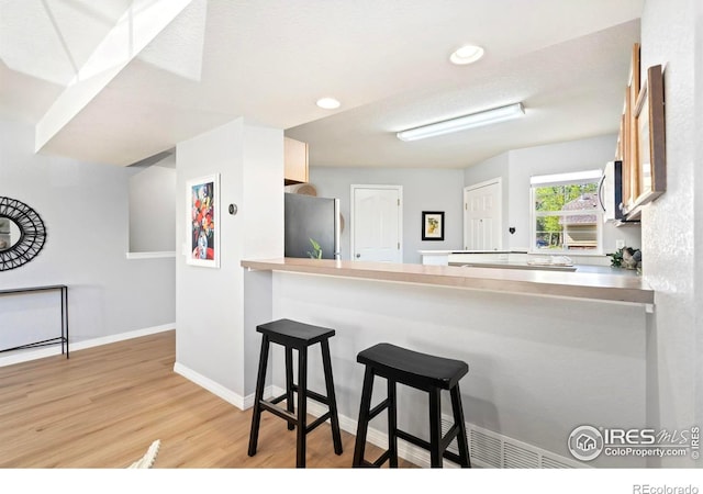 1014 Andrews Peak Dr Unit B107, Fort Collins, CO 80521 - kitchen featuring freestanding refrigerator, light wood finished floors, a peninsula, baseboards, and a breakfast bar area