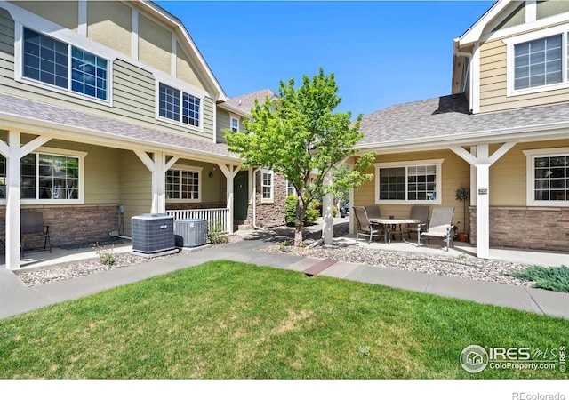 1014 Andrews Peak Dr Unit B107, Fort Collins, CO 80521 - back of property featuring stone siding, a porch, a lawn, roof with shingles, and central air condition unit