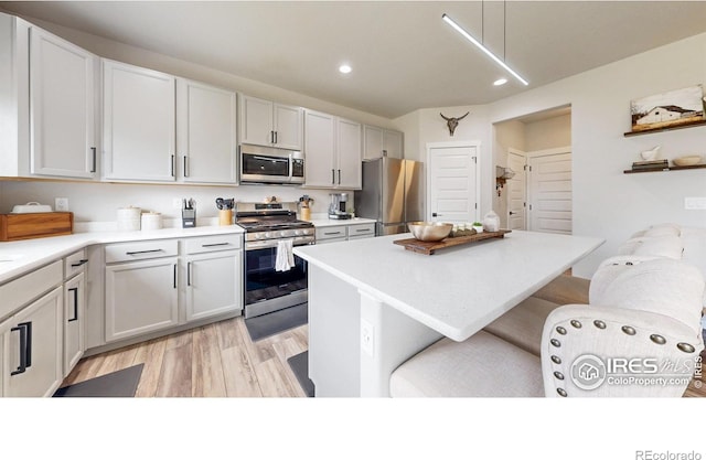 kitchen with stainless steel appliances, a breakfast bar, light wood-style flooring, recessed lighting, and light countertops