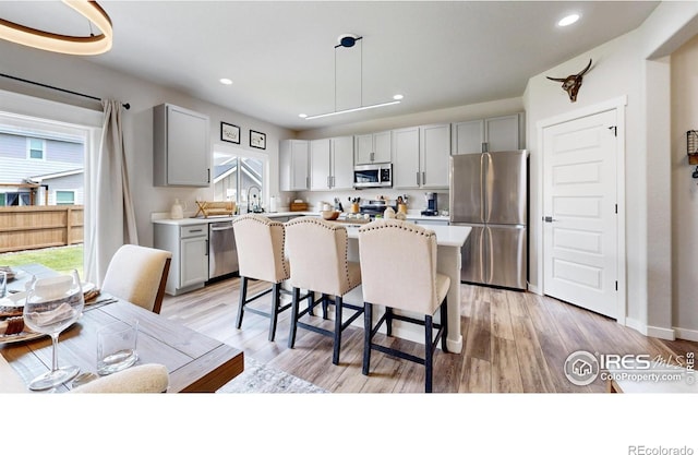 kitchen with appliances with stainless steel finishes, gray cabinets, a breakfast bar area, light countertops, and light wood-style flooring
