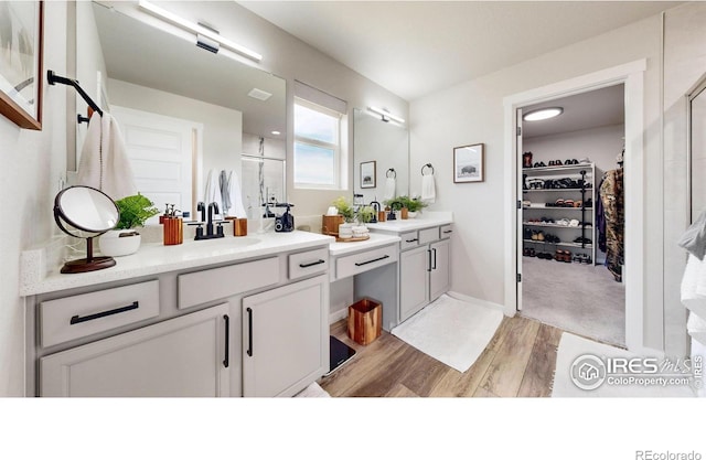 full bathroom featuring wood finished floors, a stall shower, vanity, and a walk in closet