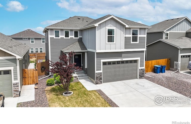 view of front of property featuring stone siding, fence, board and batten siding, an attached garage, and driveway