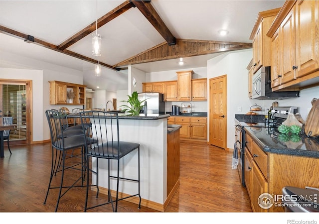 kitchen featuring appliances with stainless steel finishes, dark countertops, a breakfast bar area, and wood finished floors