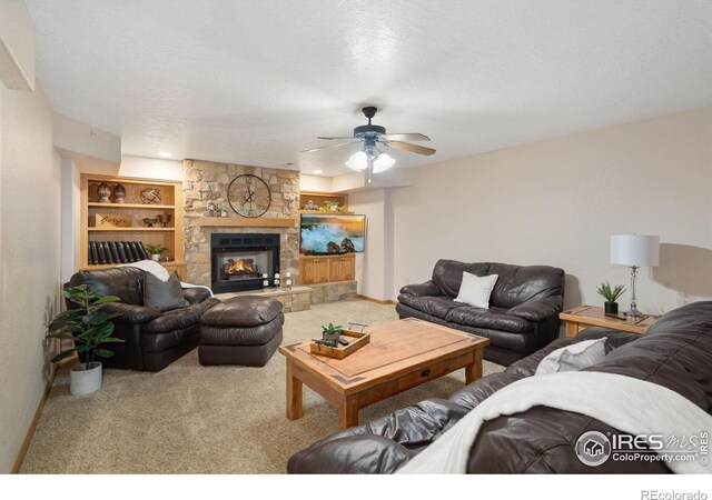 carpeted living room with a ceiling fan, baseboards, a fireplace, built in shelves, and a textured ceiling