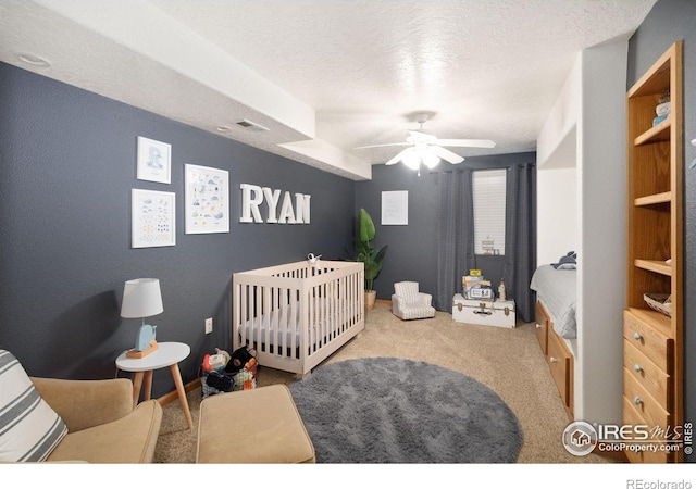 bedroom featuring carpet flooring, a nursery area, a ceiling fan, a textured ceiling, and baseboards