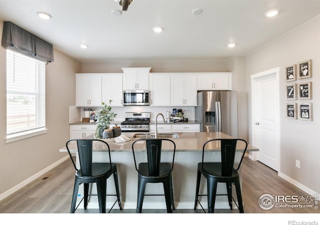 kitchen with stainless steel appliances, a sink, a kitchen bar, a center island with sink, and light wood-type flooring