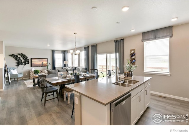 kitchen with stainless steel dishwasher, a sink, open floor plan, a chandelier, and white cabinetry