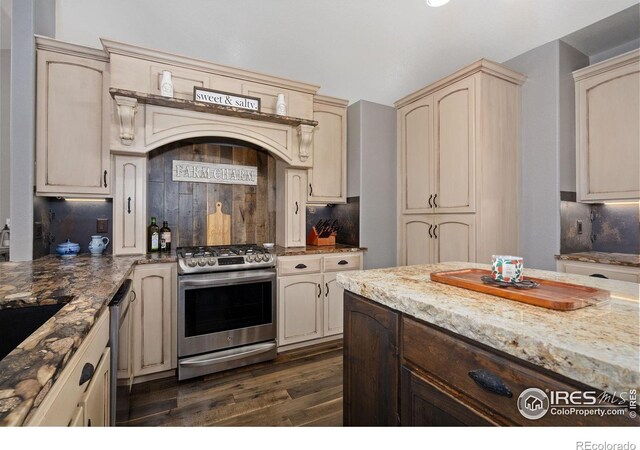 2015 Trail Ridge Dr, Severance, CO 80615 - kitchen with appliances with stainless steel finishes, cream cabinets, dark wood-style floors, decorative backsplash, and light stone counters