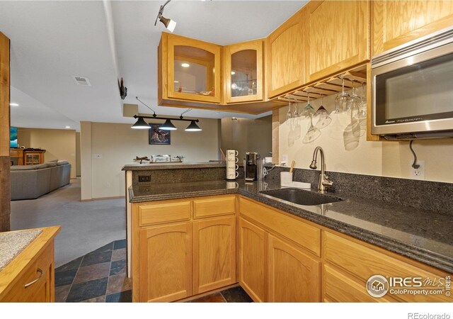 2015 Trail Ridge Dr, Severance, CO 80615 - kitchen featuring stainless steel microwave, a sink, glass insert cabinets, dark stone counters, and a peninsula