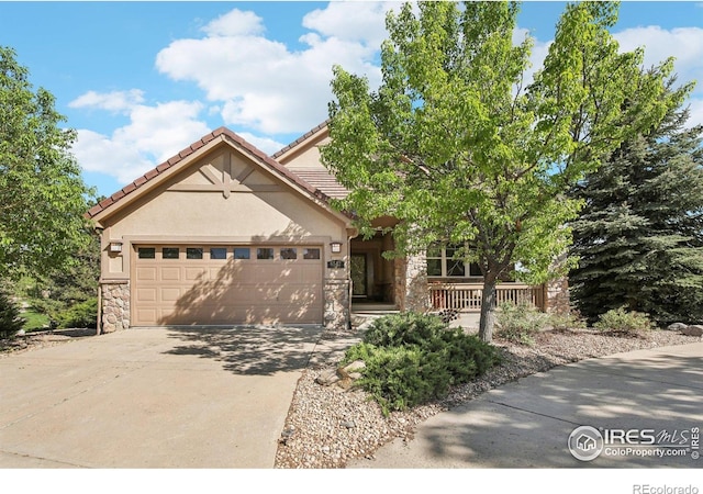view of front of house with stone siding, concrete driveway, a garage, stucco siding, and covered porch