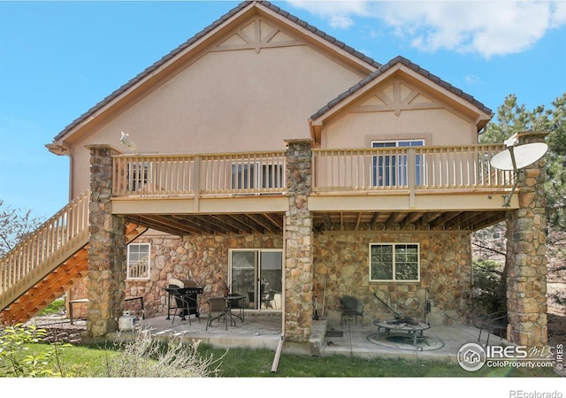 back of house featuring stone siding, a patio area, stairway, a wooden deck, and stucco siding
