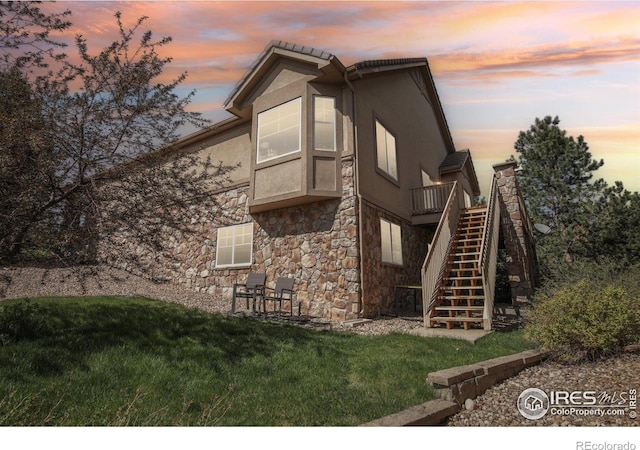 view of property exterior featuring stairway, stone siding, a yard, and stucco siding
